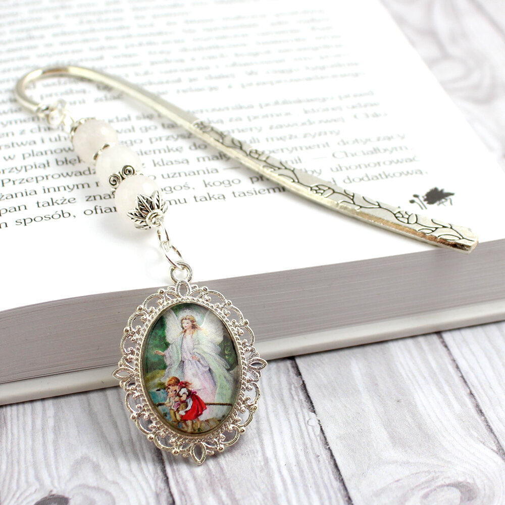 Srebrna zakładka do książki zdobiona motywem roślinnym, z zawieszką z kamieni białego jadeitu i wizerunkiem Anioła Stróża z dziećmi pod szklanym kaboszonem