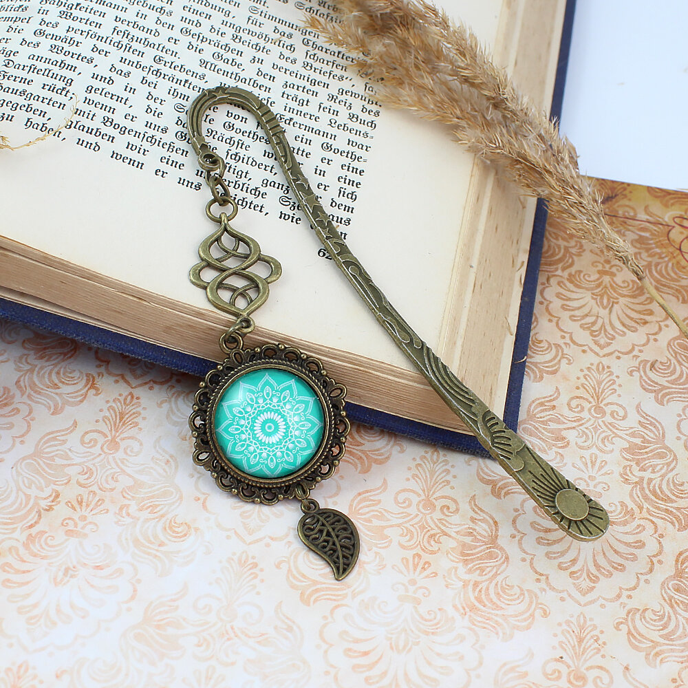 Zakładka do książki z antycznego brązu o falistym trzonie, z ozdobnym koralikiem i uspokajającą, turkusową mandalą pod szklanym kaboszonem.