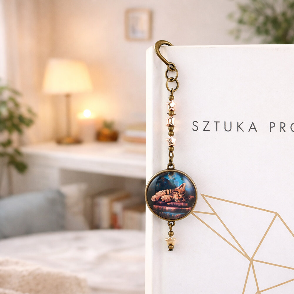 Zakładka do książki z antycznego brązu z zawieszką w kształcie gwiazdek oraz ilustracją śpiącego kota na stosie książek pod szkiełkiem.