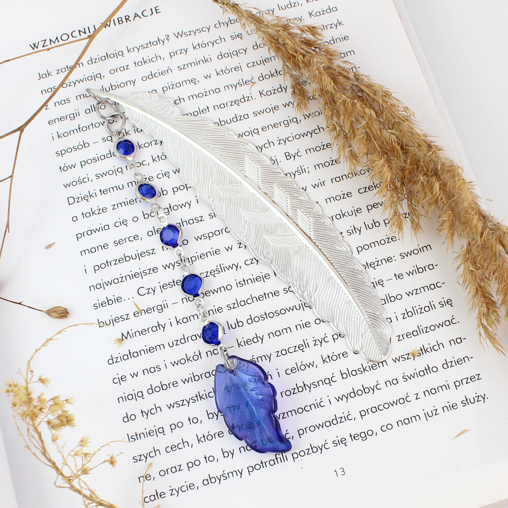 Cienka i lekka metalowa zakładka do książki w kształcie pióra, zdobiona wiszącą zawieszką z szafirowych szklanych kryształków i niebieskiego akrylowego listka, w ozdobnym pudełku.