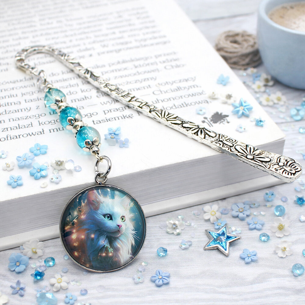 Srebrna zakładka do książki z metalowym trzonem w kwiaty i motyle, niebieskimi koralikami oraz zawieszką z autorską grafiką białego długowłosego kota