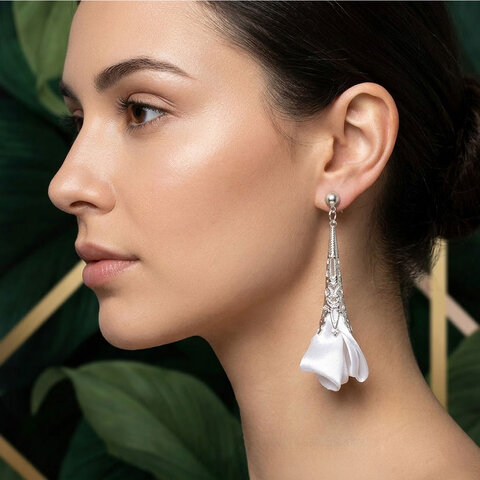 Długie, wiszące kolczyki w kształcie białych kwiatów uformowanych z tkaniny, zwieńczone ażurowym, filigranowym stożkiem w kolorze srebrnym na zapięciu typu sztyft