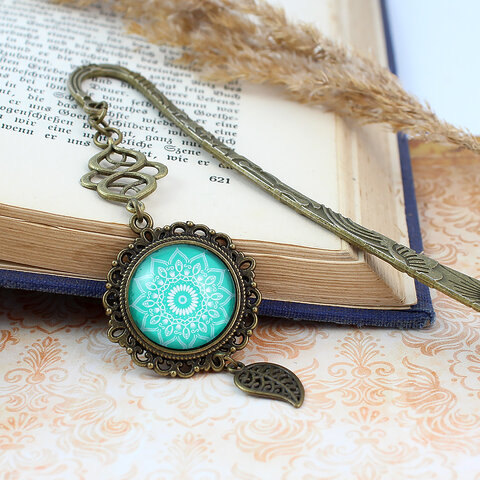 Zakładka do książki z antycznego brązu o falistym trzonie, z ozdobnym koralikiem i uspokajającą, turkusową mandalą pod szklanym kaboszonem.