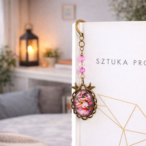 Zakładka do książki z antycznego brązu z różowymi kryształkami i owalnym szklanym kaboszonem z grafiką ptaszków i kwiatów na łące.