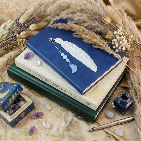 Subtelna metalowa zakładka do książki w formie piórka, zdobiona wiszącą zawieszką z opalitu w kształcie księżyca, umieszczona w pudełku prezentowym.