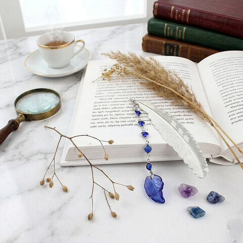 Cienka i lekka metalowa zakładka do książki w kształcie pióra, zdobiona wiszącą zawieszką z szafirowych szklanych kryształków i niebieskiego akrylowego listka, w ozdobnym pudełku.
