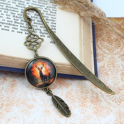 Zakładka do książki z antycznego brązu z ozdobnym falistym trzonem, zawieszką z piórkiem i ilustracją jelenia w ognistym lesie pod kaboszonem 