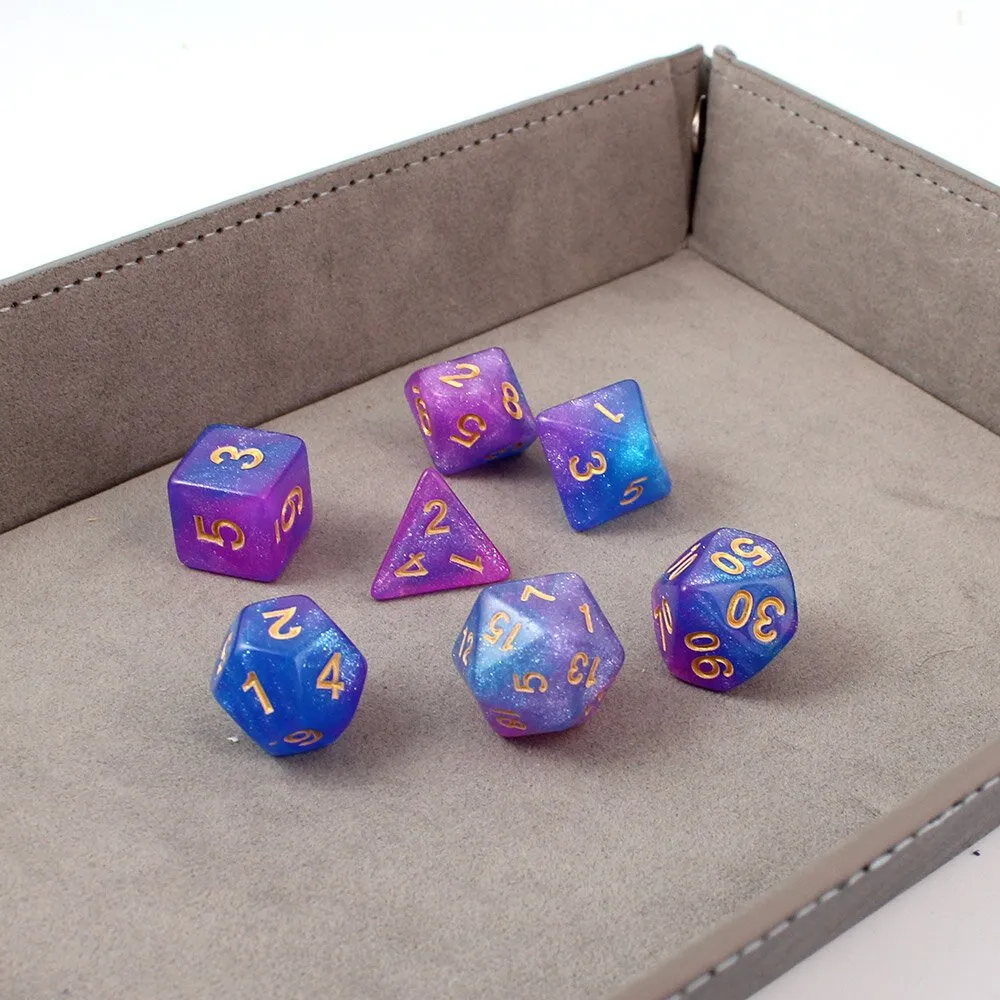 Zestaw brokatowych kości RPG Astro Dust w kolorach niebieskim i fioletowym ze złotymi cyframi.