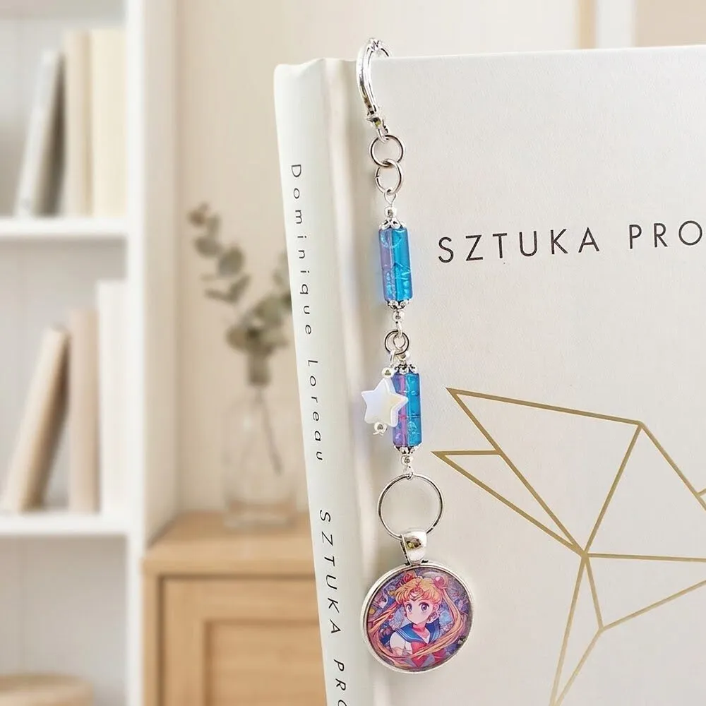 Metalowa zakładka do książki w kolorze antycznego srebra z grafiką Czarodziejki z Księżyca (Sailor Moon) pod szklanym kaboszonem, ozdobiona niebiesko-fioletowymi koralikami i gwiazdką.