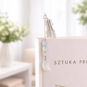 Subtelna metalowa zakładka do książki w formie piórka, zdobiona wiszącą zawieszką z opalitu w kształcie księżyca, umieszczona w pudełku prezentowym.